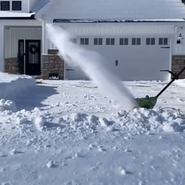 A person using a cordless electric snow shovel to clear a snow-covered driveway.